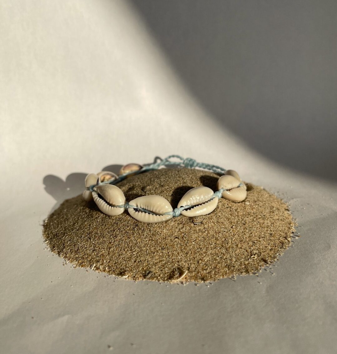 Armband met kaurischelpjes. De schelpen zijn gescheiden door een knoopje. Het draad van de armband is blauw.